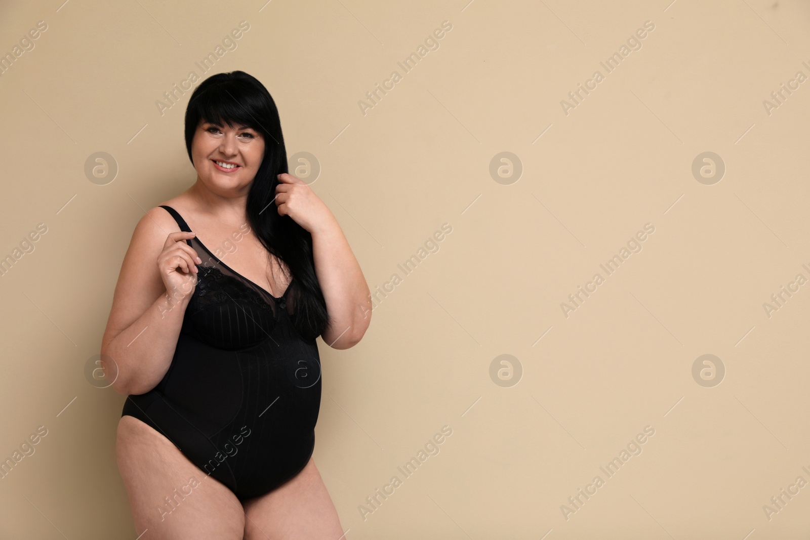 Photo of Beautiful overweight woman in black underwear on beige background, space for text. Plus-size model