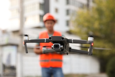 Builder operating drone with remote control at construction site, focus on quadcopter. Aerial survey