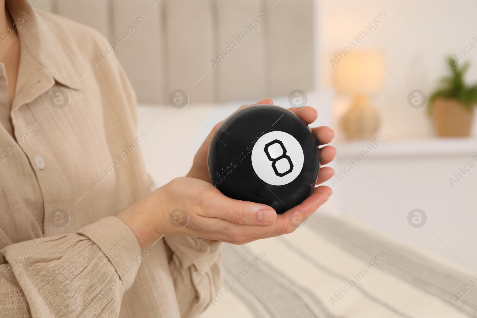 Photo of Woman holding magic eight ball indoors, closeup