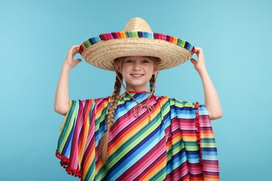 Photo of Cute girl in Mexican sombrero hat and poncho on light blue background
