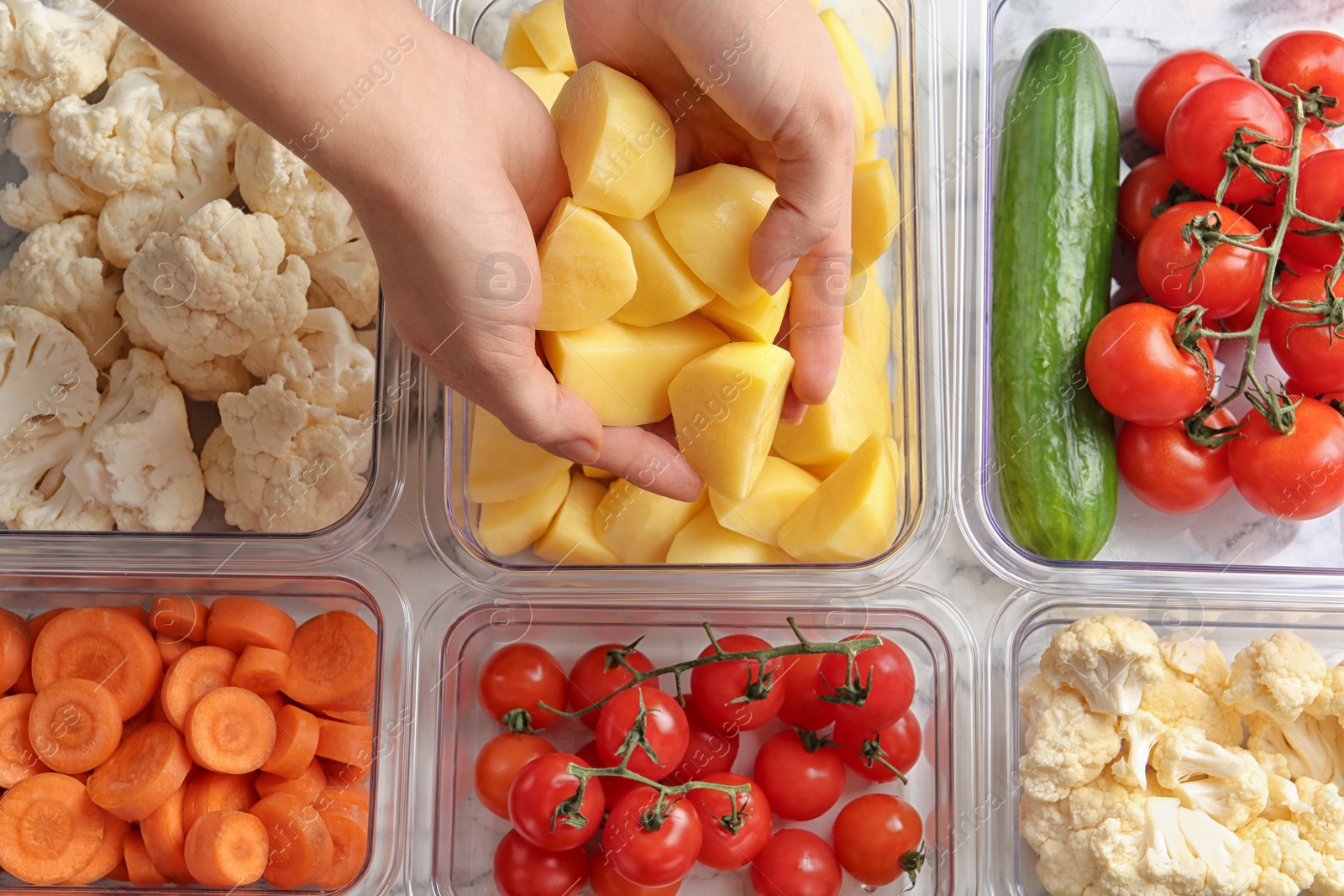 Photo of Woman putting cut potato into box and containers with raw vegetables, closeup