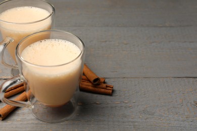 Photo of Delicious eggnog with cinnamon on grey wooden table. Space for text