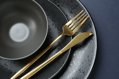 Stylish ceramic plates, bowl and cutlery on dark blue background, top view