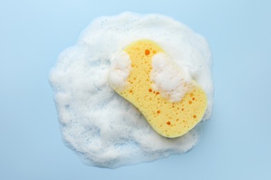 Yellow sponge with foam on light blue background, top view