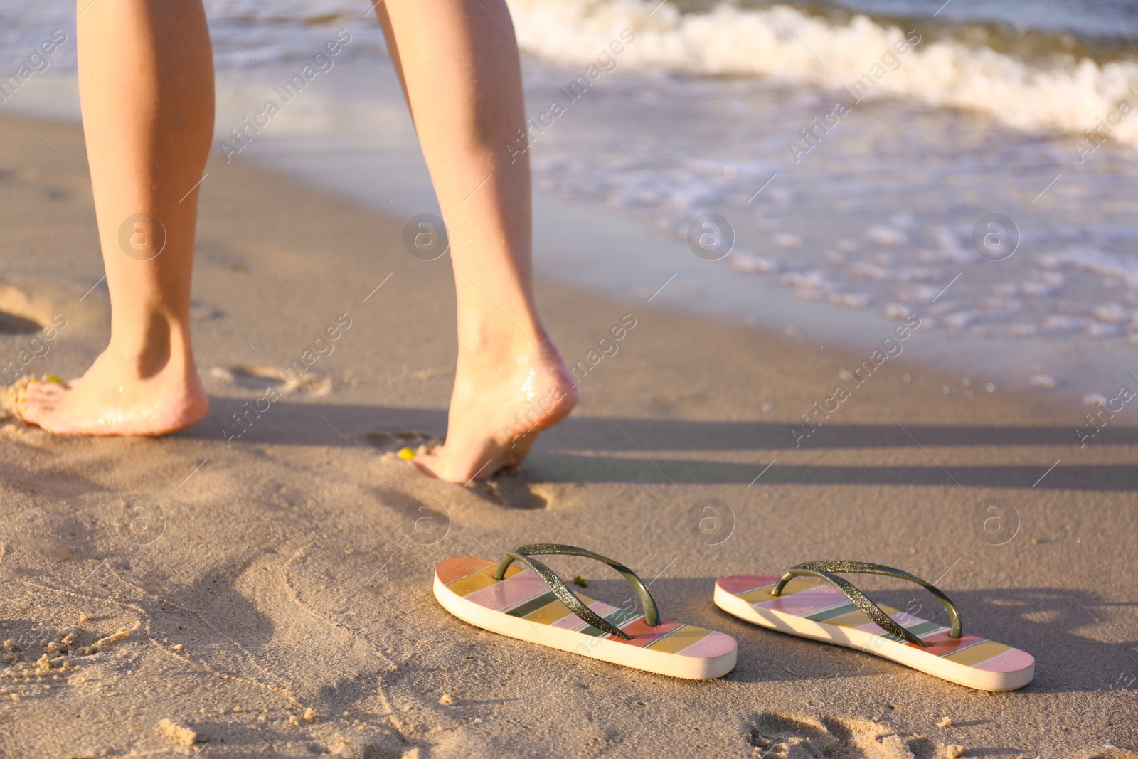 Photo of Closeup of woman and flip flops on sand near sea, space for text. Beach accessories