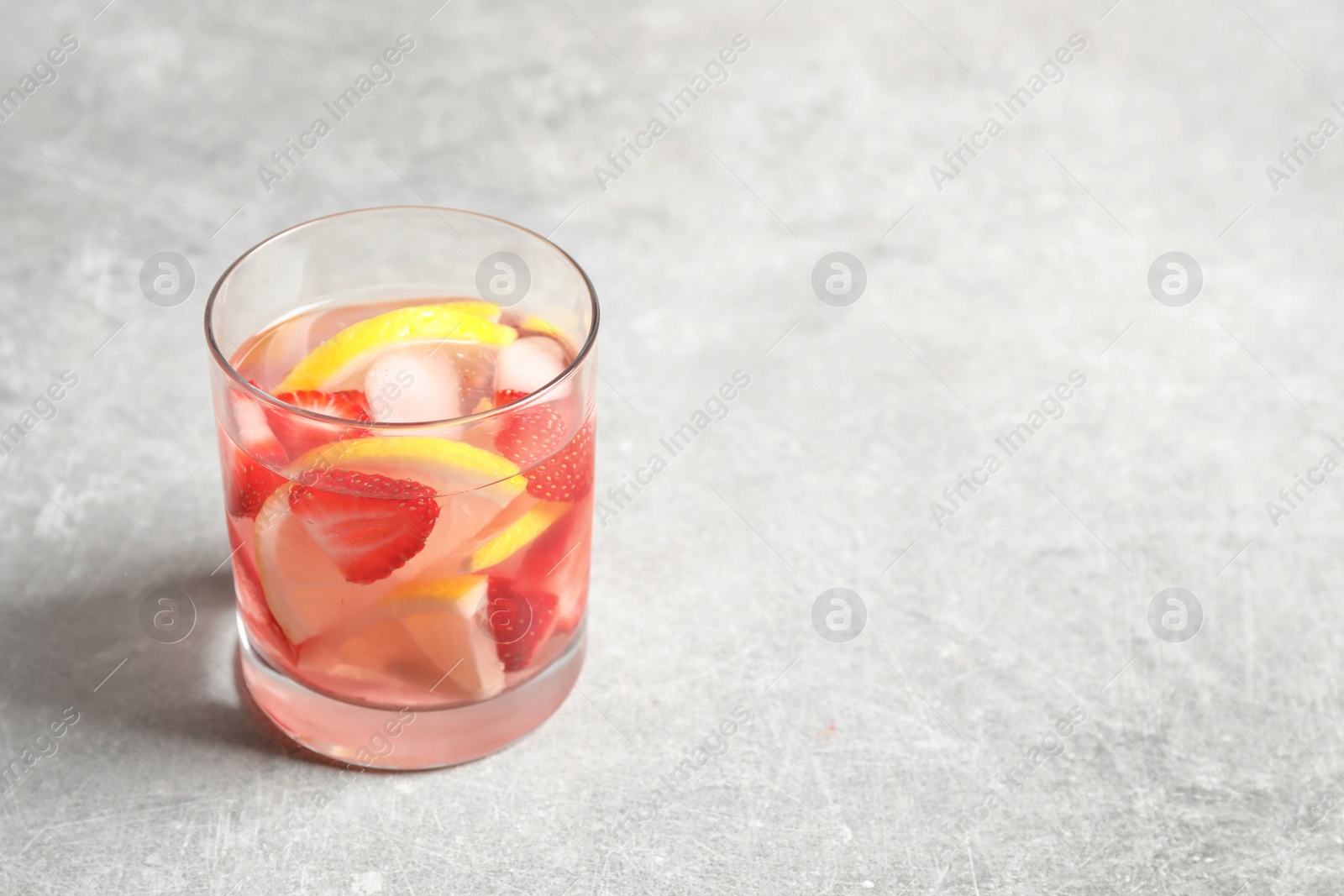 Photo of Tasty refreshing drink with strawberries and lemon on light grey table. Space for text