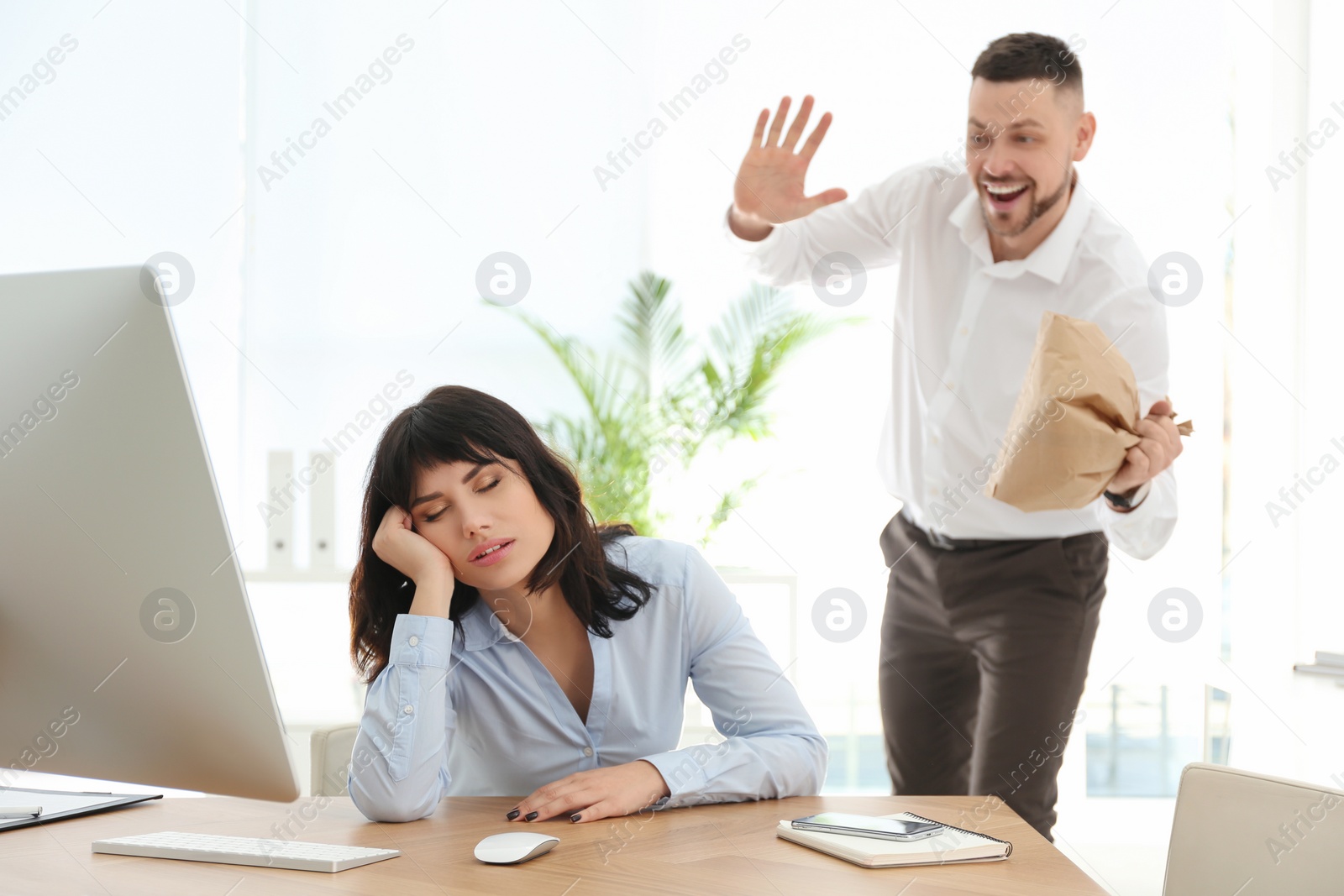 Photo of Man popping paper bag behind his sleeping colleague in office. April fool's day