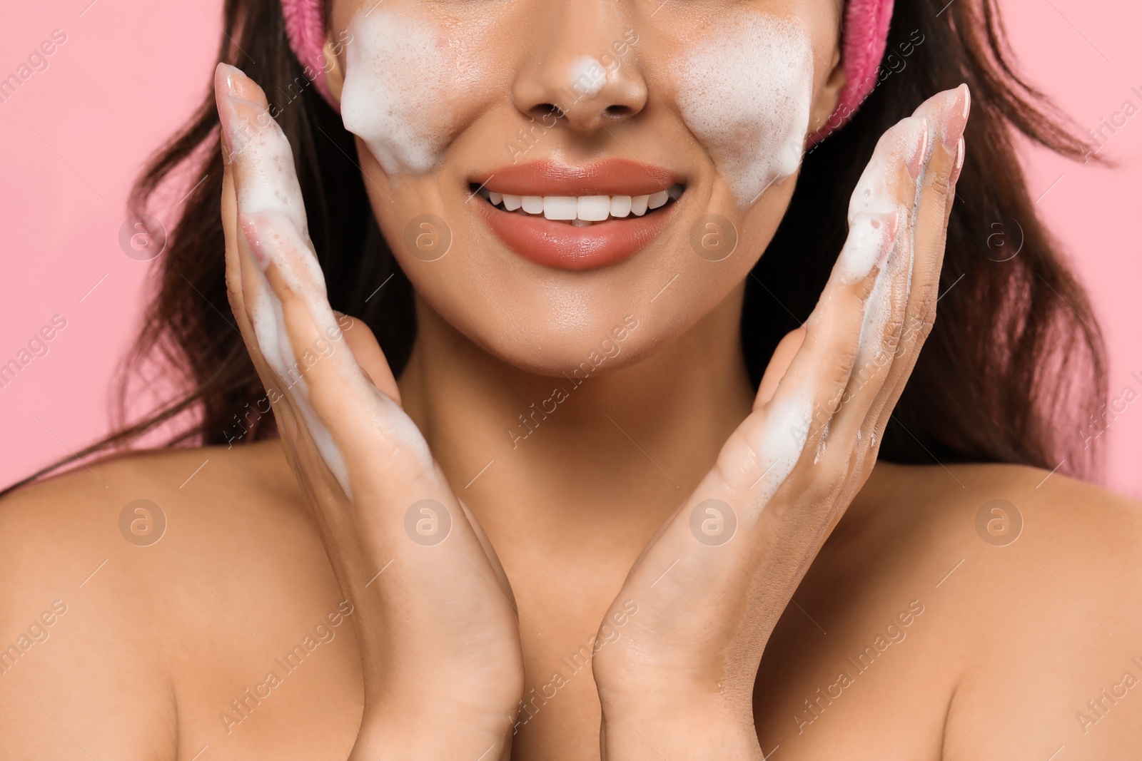 Photo of Beautiful woman applying facial cleansing foam on pink background, closeup