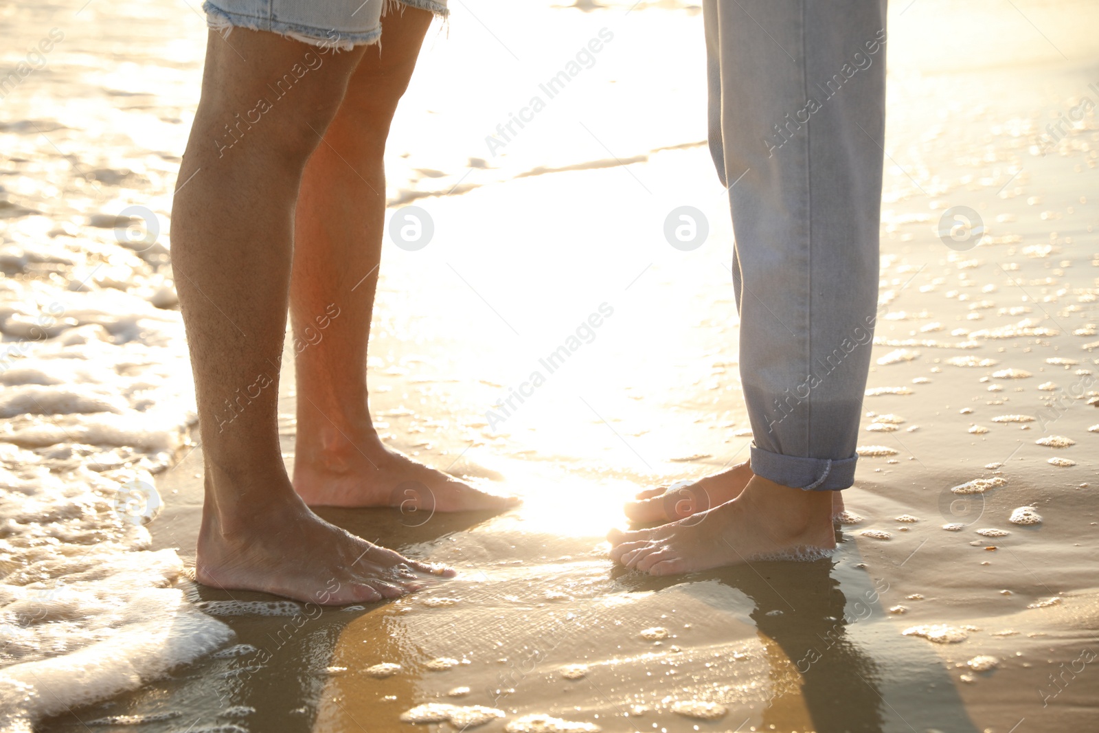 Photo of Couple on sandy beach near sea at sunset, closeup of legs