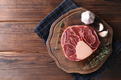 Photo of Piece of raw beef meat, thyme and garlic on wooden table, top view. Space for text