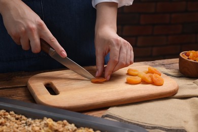 Photo of Making granola. Woman cutting dry apricots at wooden table, closeup