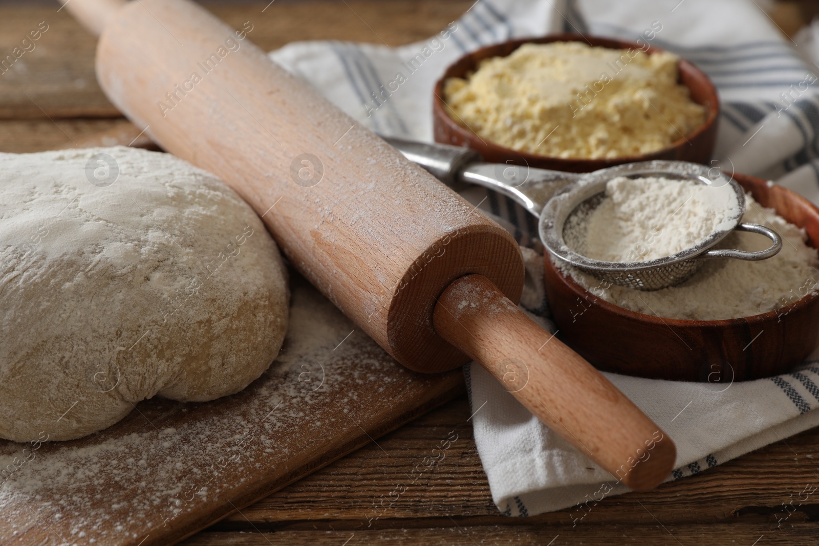 Photo of Rolling pin, flour and dough on wooden table, closeup