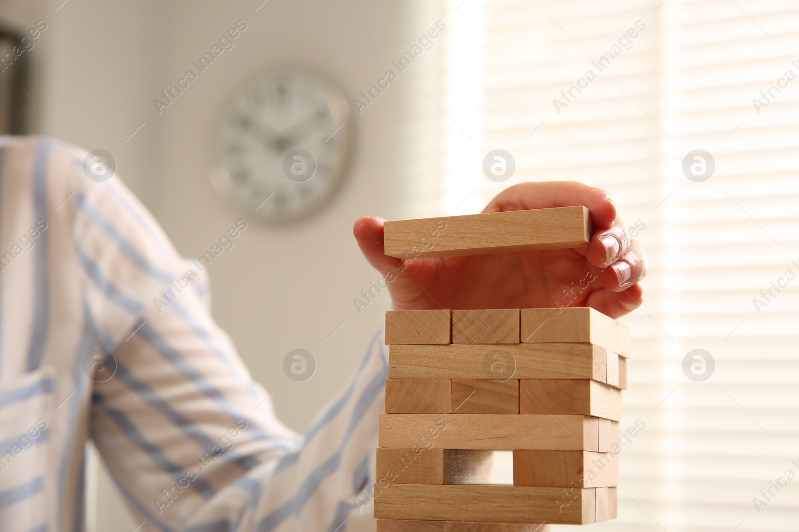 Photo of Playing Jenga. Woman building tower with wooden blocks indoors, closeup