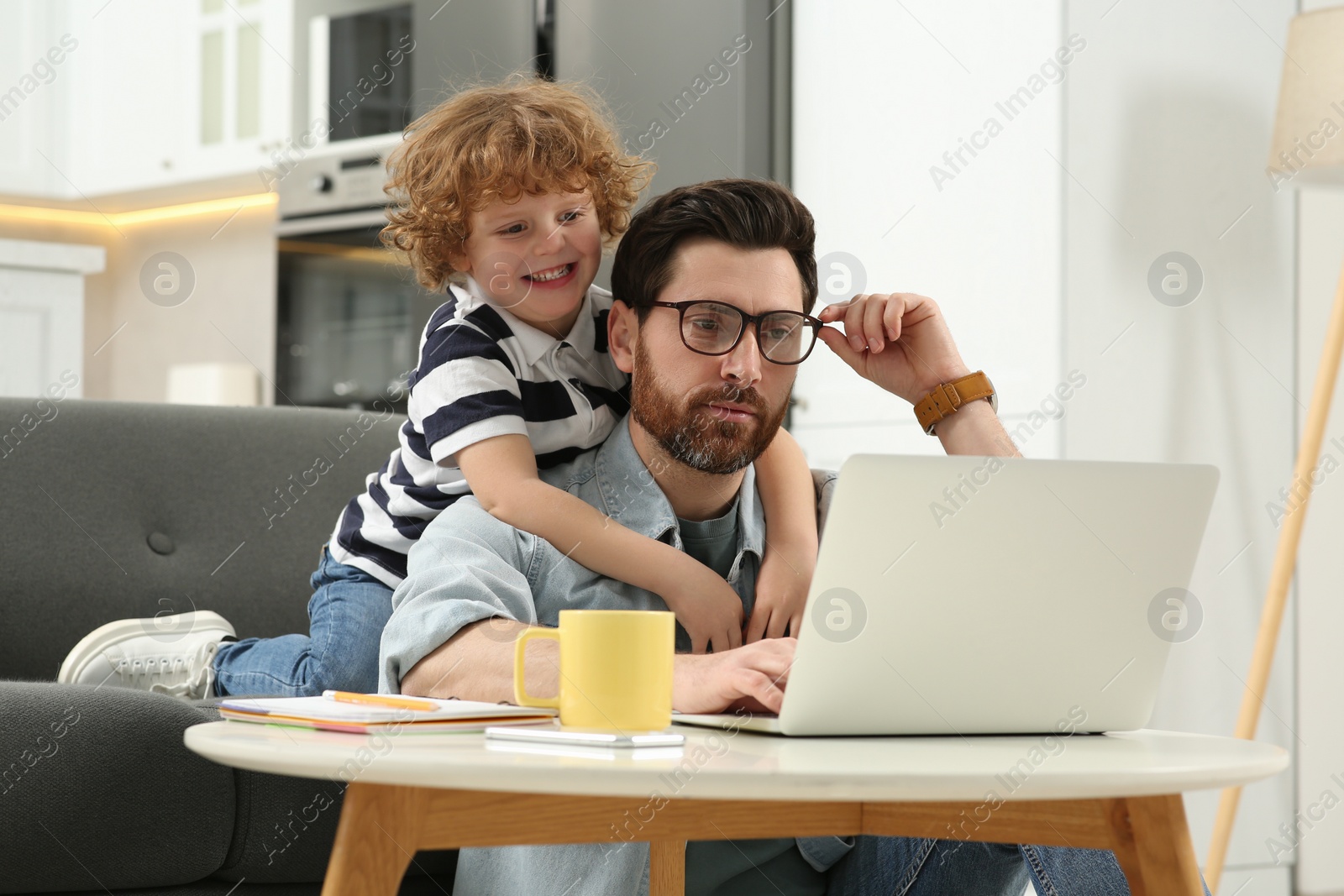 Photo of Man with laptop working remotely at home. Father and son at desk