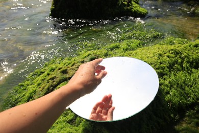 Photo of Woman with round mirror on seaweed near sea, closeup