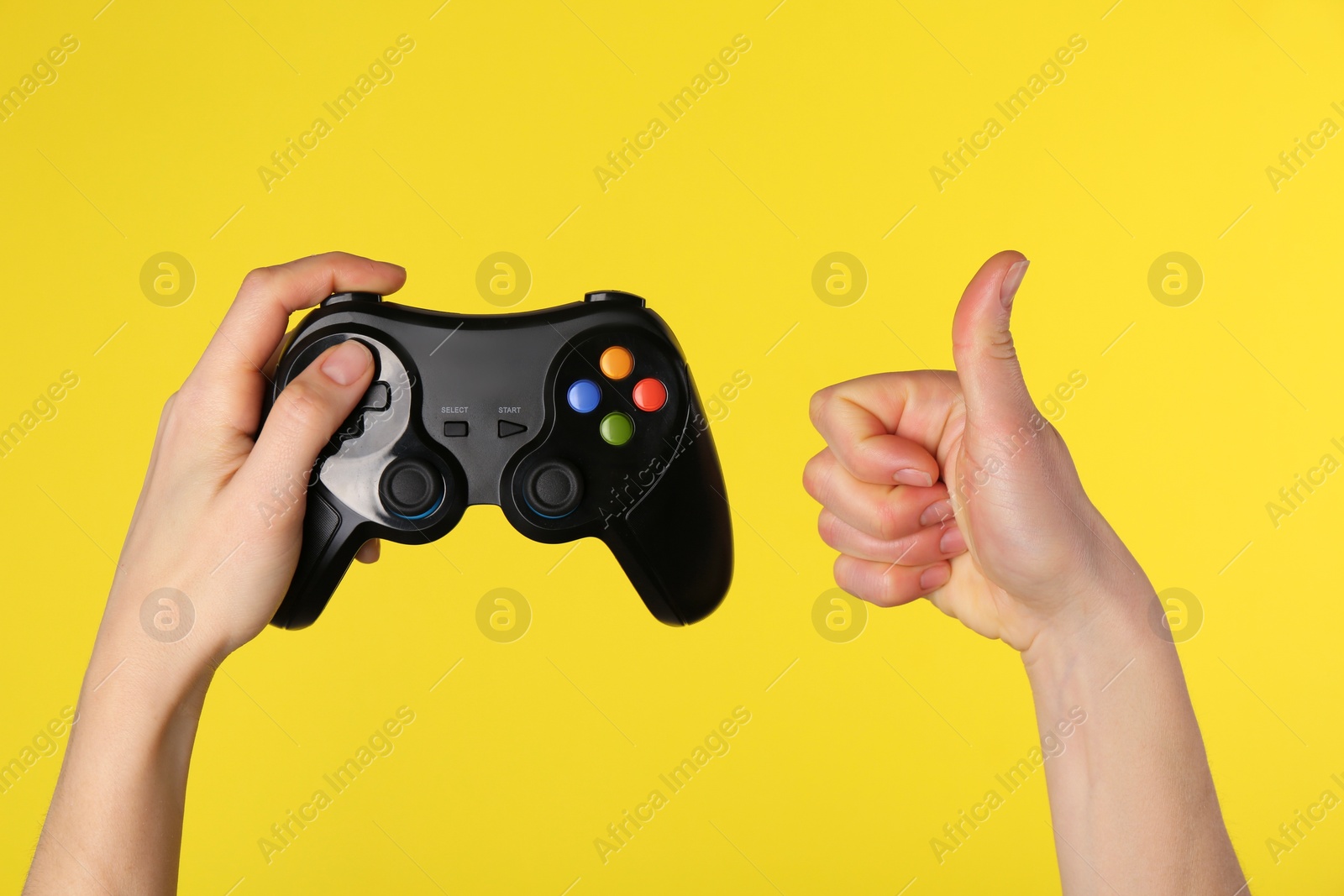 Photo of Woman with game controller showing thumbs up on yellow background, closeup