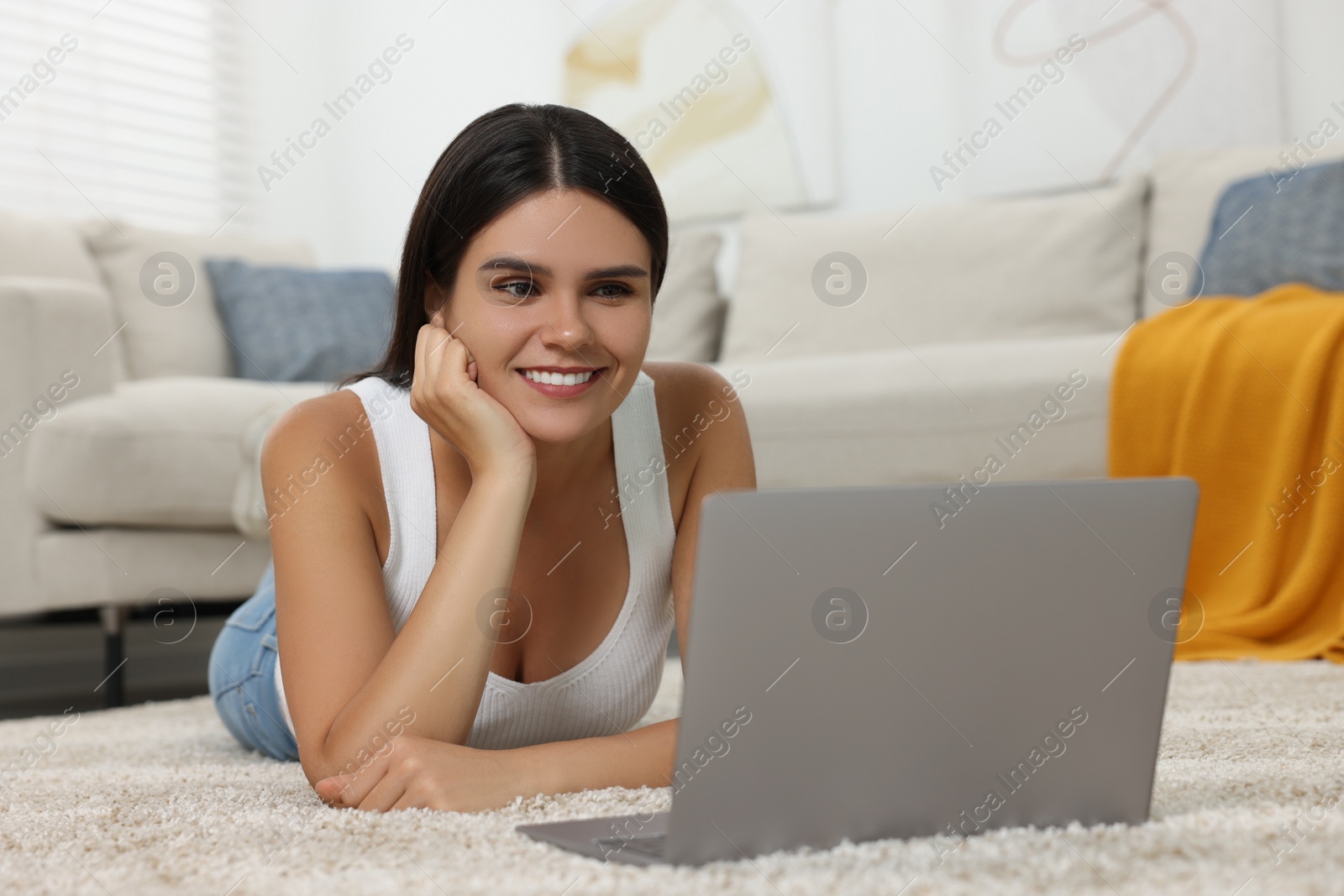 Photo of Happy young woman having video chat via laptop on floor in living room