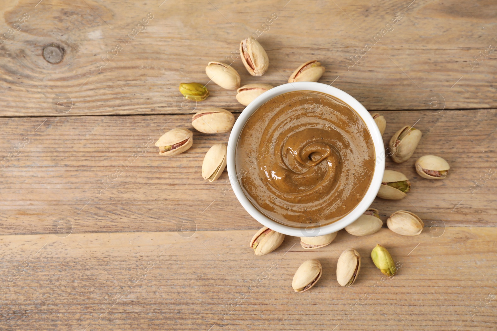 Photo of Delicious nut butter in bowl and pistachios on wooden table, top view. Space for text