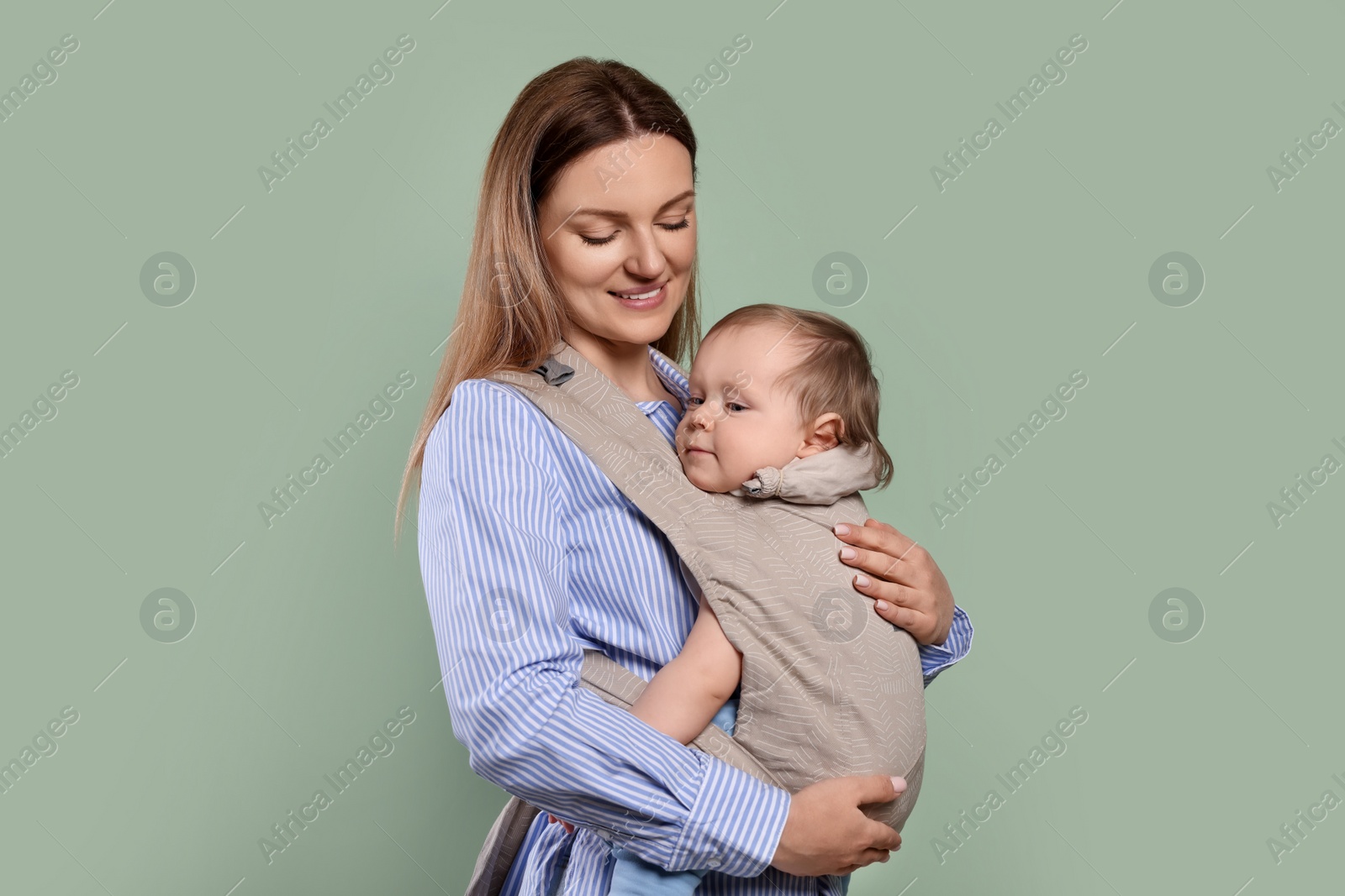 Photo of Mother holding her child in sling (baby carrier) on olive background