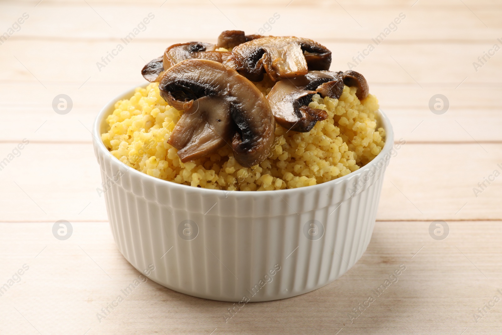 Photo of Tasty millet porridge and mushrooms in bowl on light wooden table, closeup