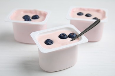 Photo of Plastic cups with tasty yogurts and blueberries on white wooden table