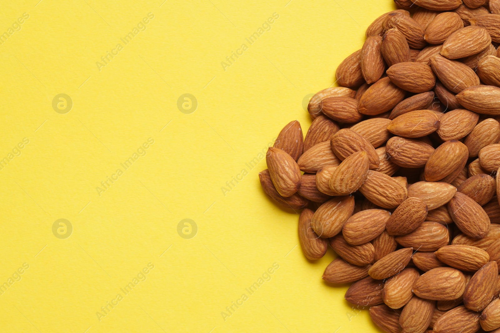 Photo of Delicious raw almonds on yellow background, flat lay. Space for text