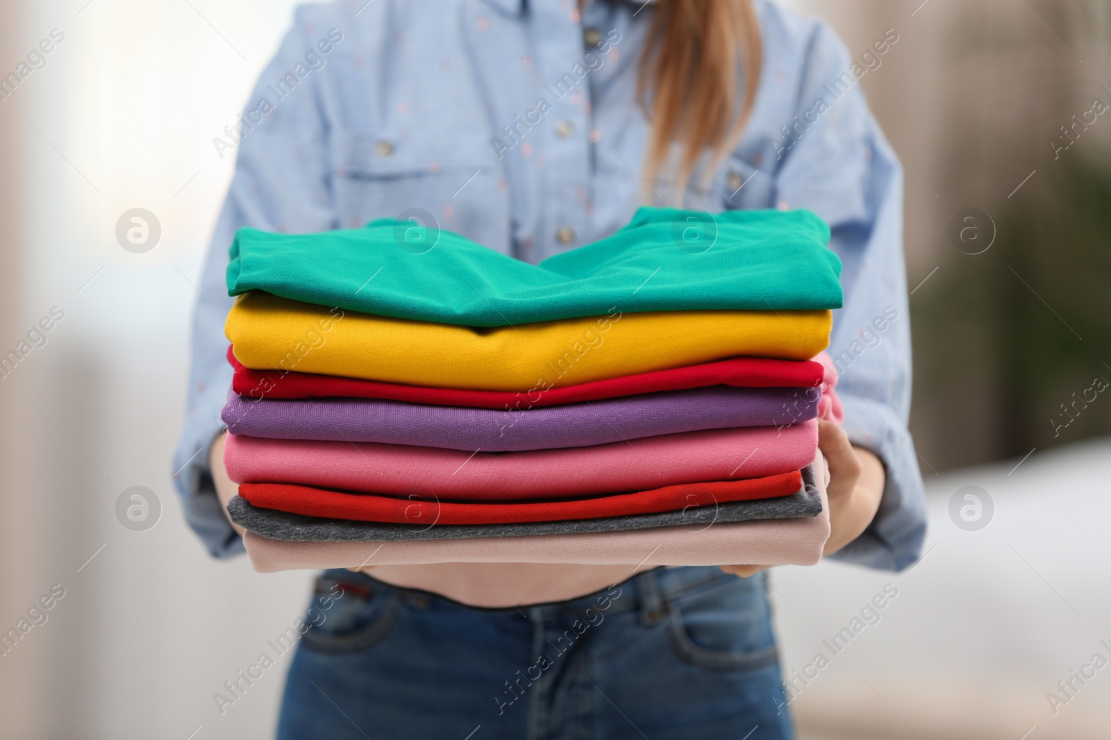 Photo of Woman holding folded clean clothes indoors, closeup. Laundry day