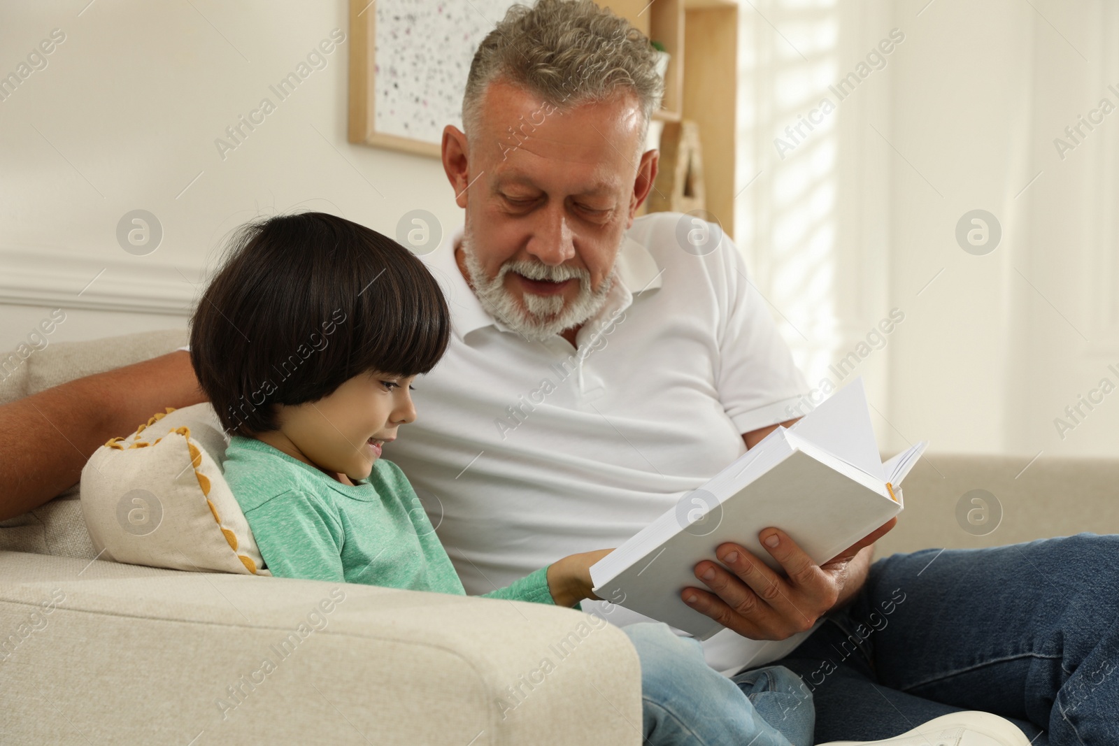 Photo of Happy grandfather with his grandson reading book together at home