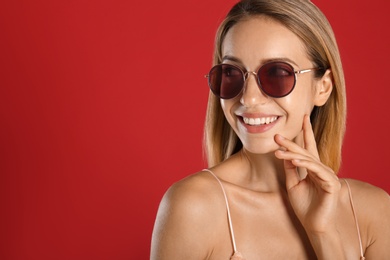 Photo of Beautiful woman in stylish sunglasses on red background. Space for text