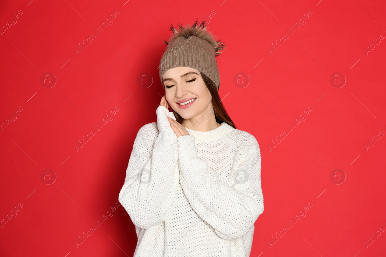 Photo of Young woman wearing warm sweater and hat on red background. Winter season