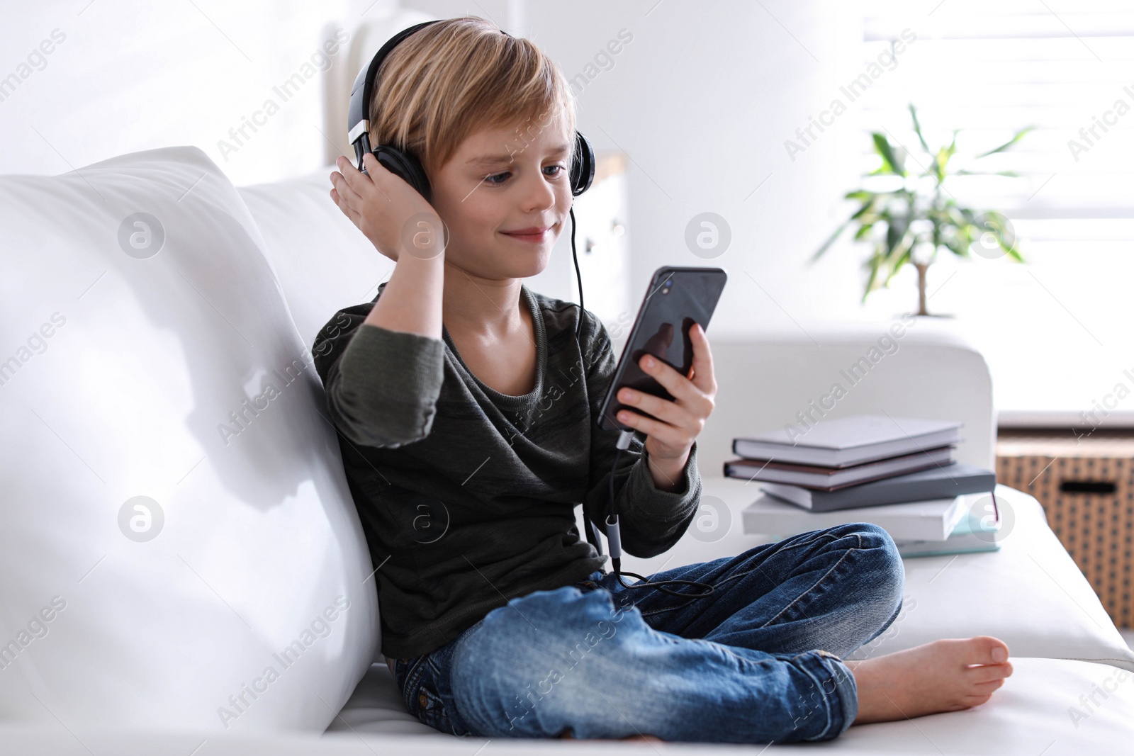 Photo of Cute little boy with headphones and smartphone listening to audiobook at home