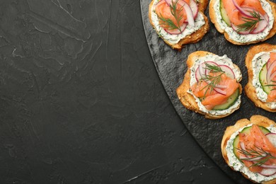 Photo of Tasty canapes with salmon, cucumber, radish and cream cheese on black table, top view. Space for text