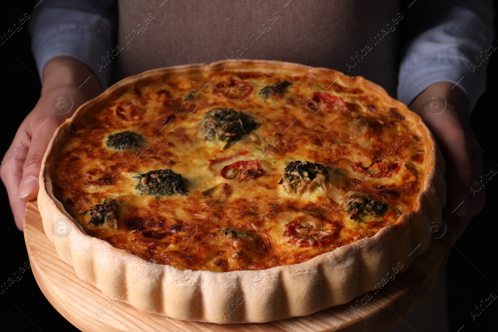 Photo of Woman holding delicious homemade vegetable quiche on black background, closeup