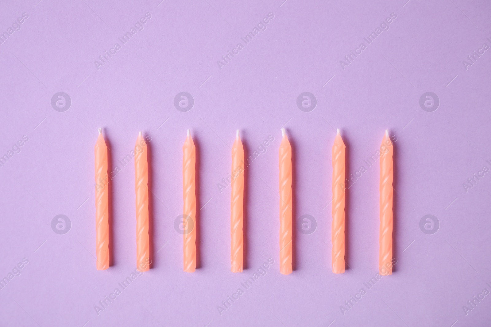 Photo of Orange birthday candles on lilac background, top view
