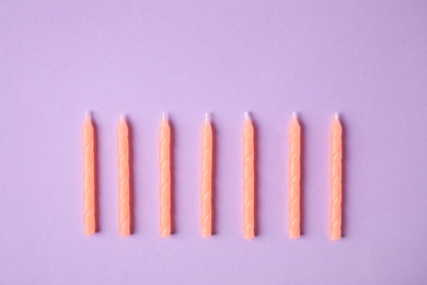 Photo of Orange birthday candles on lilac background, top view