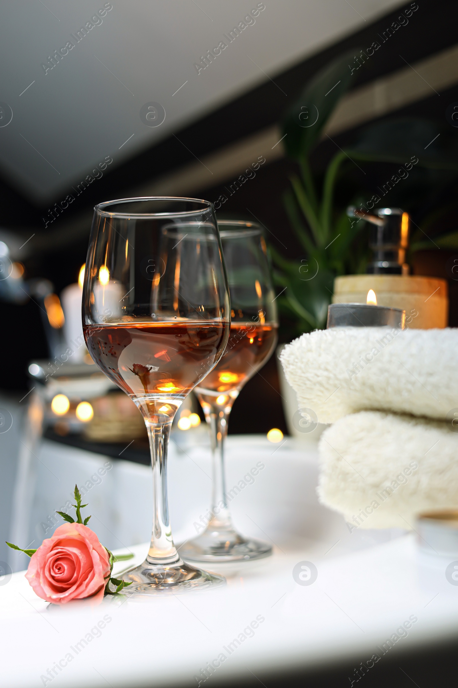 Photo of Bathtub with glasses of wine and candles indoors. Romantic atmosphere.