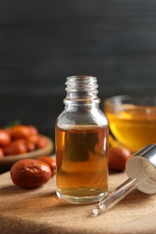 Photo of Glass bottle with jojoba oil and seeds on wooden board