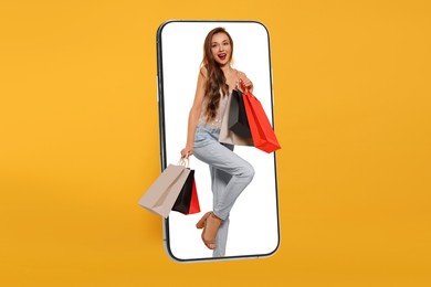 Image of Online shopping. Happy woman with paper bags walking out from smartphone on orange background