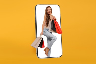 Online shopping. Happy woman with paper bags walking out from smartphone on orange background