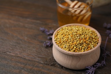 Photo of Fresh bee pollen granules in bowl, lavender and honey on wooden table, closeup. Space for text