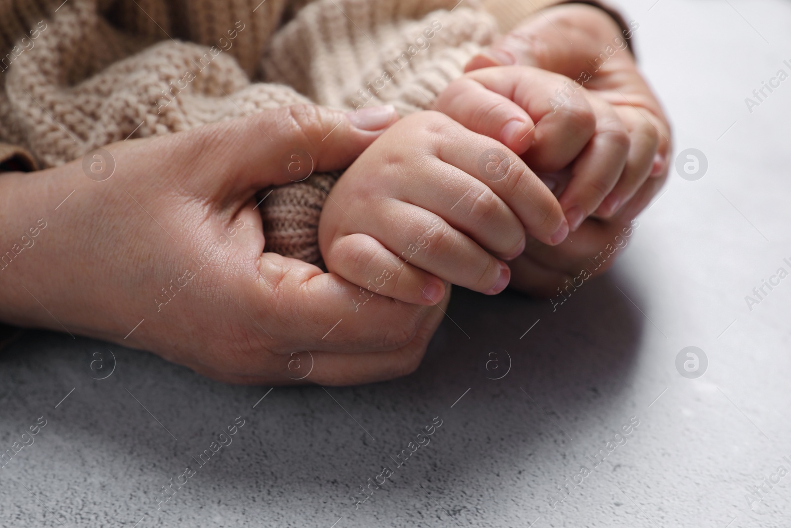 Photo of Woman holding hands with her little daughter at light grey table, closeup