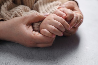 Woman holding hands with her little daughter at light grey table, closeup
