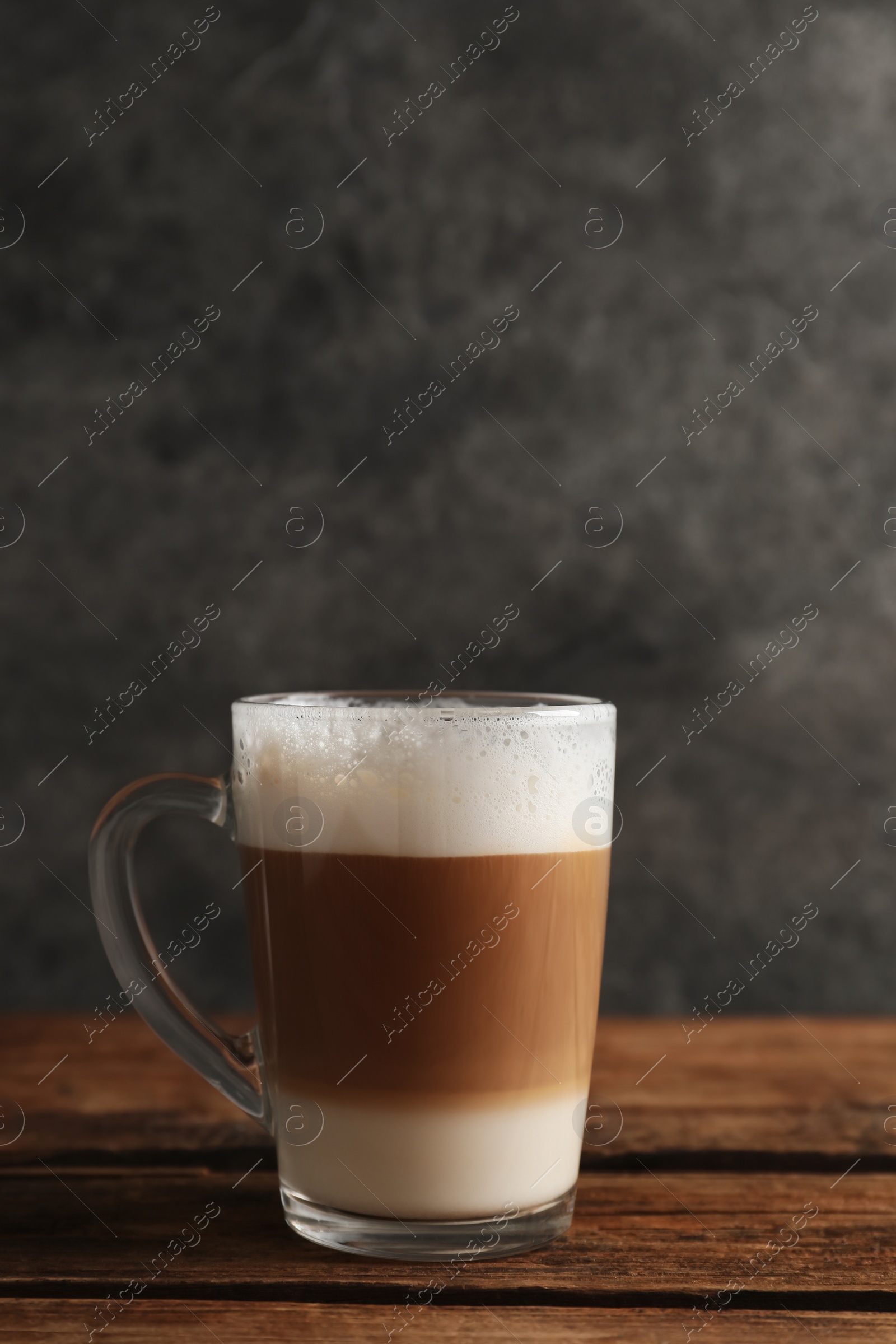 Photo of Glass cup of delicious layered coffee on wooden table against grey background, space for text