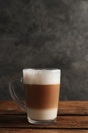 Photo of Glass cup of delicious layered coffee on wooden table against grey background, space for text