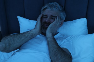 Photo of Mature man suffering from headache in bed at night