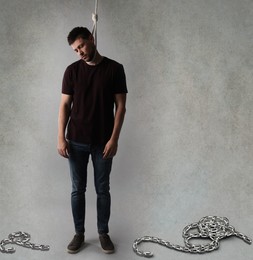 Depressed man with rope noose on neck against light grey background