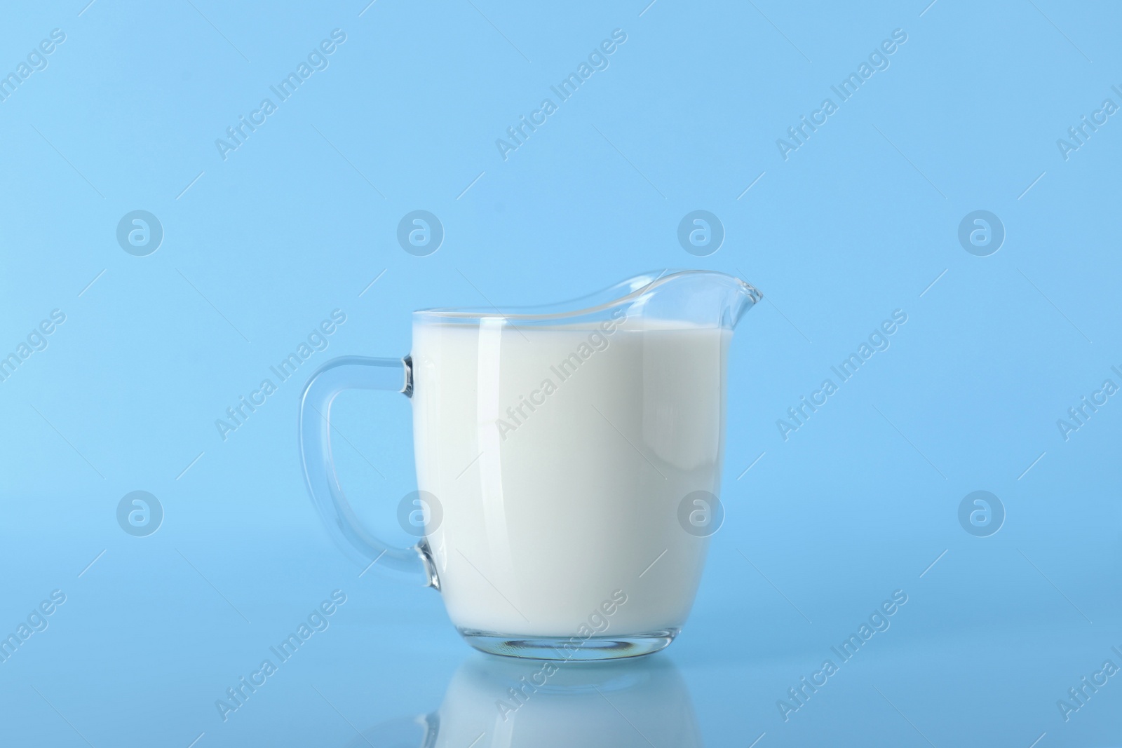 Photo of Jug of fresh milk on light blue background