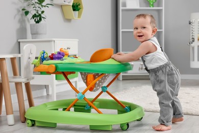 Photo of Cute baby making first steps with toy walker at home