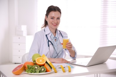 Nutritionist with glass of juice and laptop at desk in office