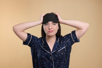 Photo of Tired young woman with sleep mask on beige background. Insomnia problem